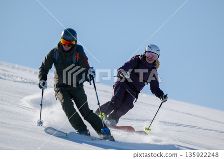 Two skiers carving powder on a snowy slope in an off-piste freeride adventure Two skiers carving powder on a snowy slope in an off-piste freeride adventure 135922248