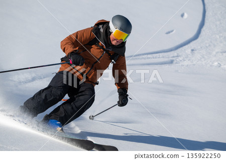 Skier carving through powder on a bright winter slope with helmet and goggles 135922250