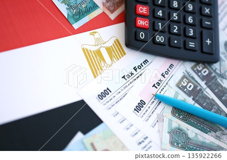 Egyptian pound money bills and calculator with tax form on flag close up. Taxation and accounting concept Egyptian pound money bills and calculator with tax form on flag close up. Taxation and accounting concept 135922266