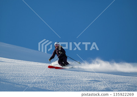 Skier carving downhill on a clear blue day in fresh powder snow during bright winter sun 135922269