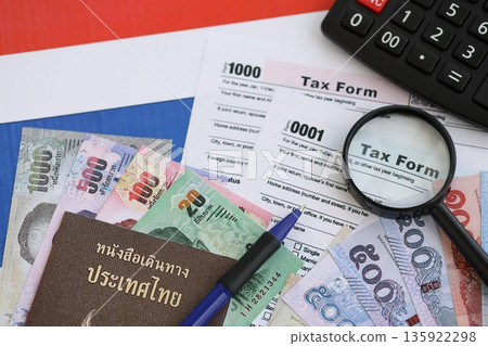 Thai baht money bills and calculator with tax form on flag close up. Taxation and accounting concept Thai baht money bills and calculator with tax form on flag close up. Taxation and accounting concept 135922298