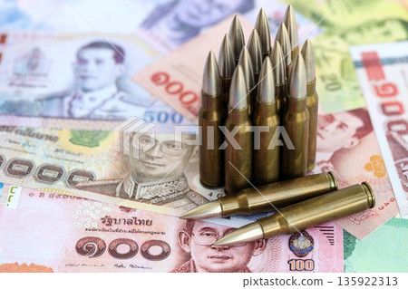 Thai baht currency money bills and rifle bullets close up. The concept of warfare and gun selling Thai baht currency money bills and rifle bullets close up. The concept of warfare and gun selling 135922313