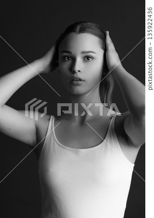 Woman posing with hands on head in black and white studio Woman posing with hands on head in black and white studio 135922436