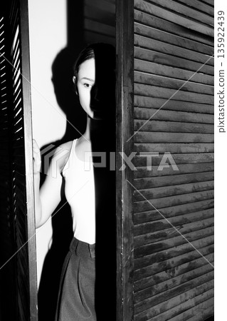 Woman revealing face from shadows by wooden shutters 135922439