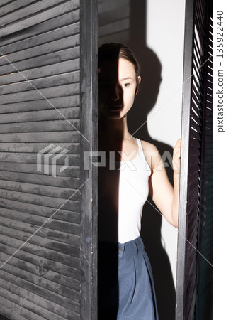 Woman peeking through shutters with shadow play 135922440