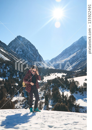 Woman hiking on a snowy mountain trail with clear blue sky and bright sun. Winter trekking adventure in a valley. Mountain landscape. Woman hiking on a snowy mountain trail with clear blue sky and bright sun. Winter trekking adventure in a valley. Mountain landscape. 135922491