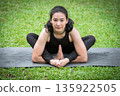 Asian woman practicing yoga on mat in outdoor park. 135922505