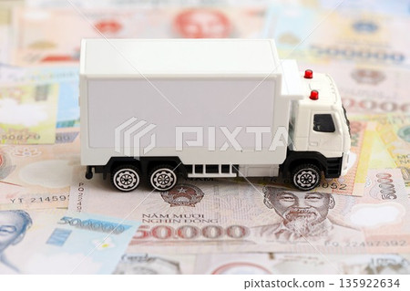 Vietnamese dong currency money bills and toy delivery truck close up. The concept of delivery and logistics Vietnamese dong currency money bills and toy delivery truck close up. The concept of delivery and logistics 135922634