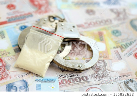 Vietnamese dong currency money bills and cocaine pack with handcuffs close up. The concept of drug crimes 135922638
