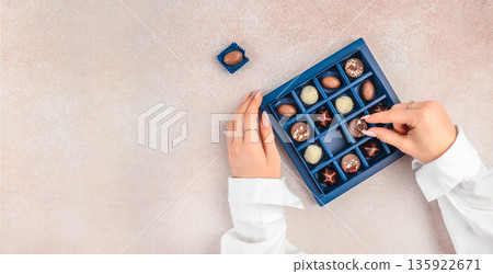 Hands selecting chocolate praline from luxury gift box with copy space Hands selecting chocolate praline from luxury gift box with copy space 135922671