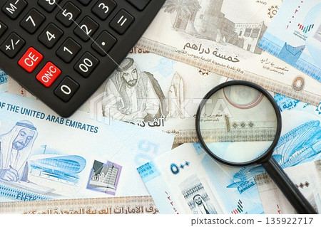 United Arab Emirates dirham currency money bills and calculator with magnifying glass close up. The concept of taxation and money count United Arab Emirates dirham currency money bills and calculator with magnifying glass close up. The concept of taxation and money count 135922717