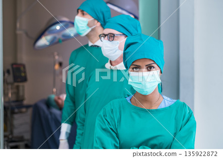 Portrait of Multi-Cultural surgical doctor team in green coat, arms crossed, and standing in front of emergency surgical room. Look at camera. Portrait of Multi-Cultural surgical doctor team in green coat, arms crossed, and standing in front of emergency surgical room. Look at camera. 135922872
