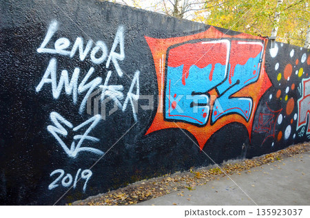 The old wall decorated with paint stains in the style of street art culture. Colorful background of full graffiti painting artwork with bright aerosol outlines on wall. Colored background texture The old wall decorated with paint stains in the style of street art culture. Colorful background of full graffiti painting artwork with bright aerosol outlines on wall. Colored background texture 135923037