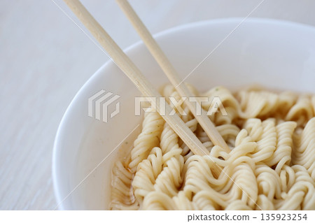 Bowl of instant cooking noodles with wooden chopsticks on white wooden table close up 135923254