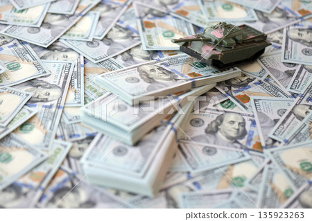 Toy tank on US hundred dollar bills banknotes close up. The concept of war costs, military spending and economic crisis Toy tank on US hundred dollar bills banknotes close up. The concept of war costs, military spending and economic crisis 135923263