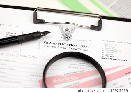Thailand Visa application form on A4 tablet lies on office table with pen and magnifying glass close up 135923389