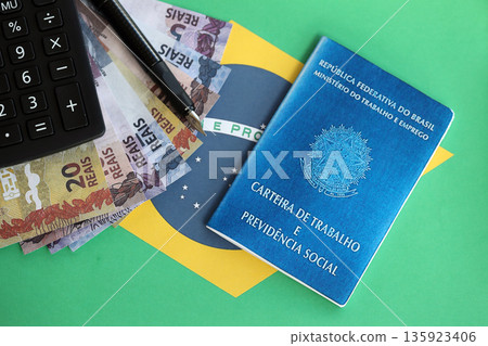 Brazilian work card and social security blue book and reais money bills with calculator and pen on flag of Federative Republic of Brazil close up Brazilian work card and social security blue book and reais money bills with calculator and pen on flag of Federative Republic of Brazil close up 135923406