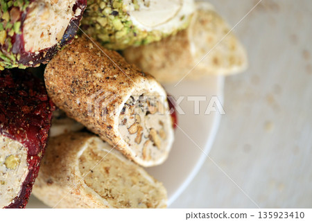 Many rolls of turkish delight with different flavors and fillings in white plate on table. Cuts of Turk Lokumu sweets 135923410