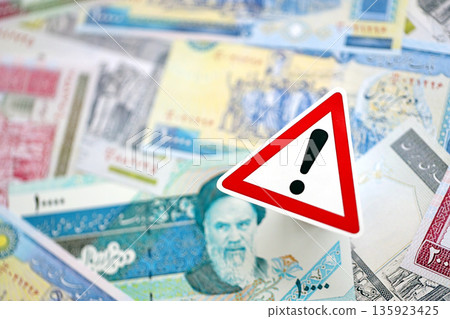 Small exclamation sign lies on pile of iranian money close up. Sanctions, ban or embargo concept Small exclamation sign lies on pile of iranian money close up. Sanctions, ban or embargo concept 135923425