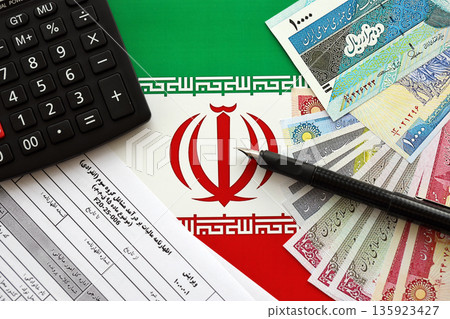 Iranian annual income tax return form F20-25-006 ready to fill on table with pen, calculator and iranian money on flag close up 135923427