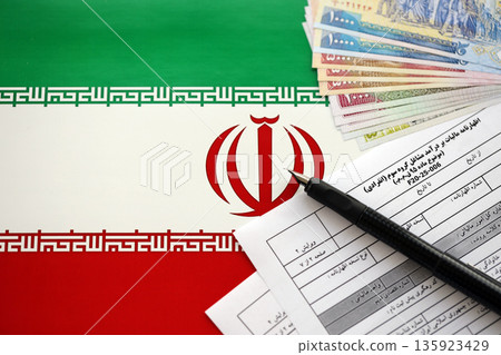 Iranian annual income tax return form F20-25-006 ready to fill on table with pen and iranian money on flag close up 135923429