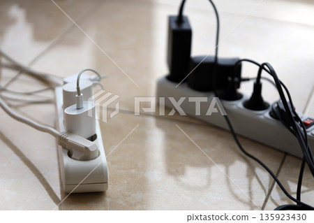Overloaded power boards. Power strips with different electrical plugs on white floor. Concept of risk danger overloaded current electrical Overloaded power boards. Power strips with different electrical plugs on white floor. Concept of risk danger overloaded current electrical 135923430