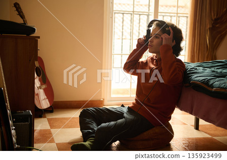 Teenage Boy With Headphones Exploring Music In A Cozy Bedroom Studio Setup At Home 135923499