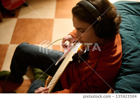 Teen Guitar Player With Headphones Focused On Music In A Cozy Room Teen Guitar Player With Headphones Focused On Music In A Cozy Room 135923504