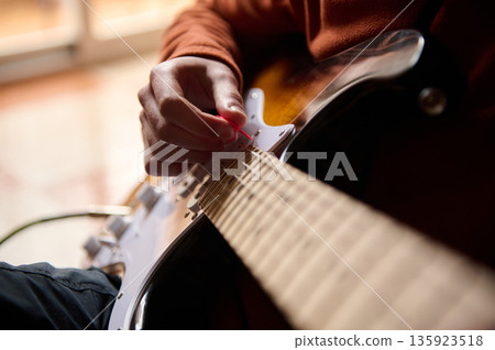 Teenage Guitarist Practices on Electric Guitar With Pick, Close-Up of Hand and Strings Teenage Guitarist Practices on Electric Guitar With Pick, Close-Up of Hand and Strings 135923518