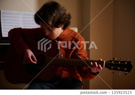 Teenage Boy Playing Acoustic Guitar In Warm Room, Focused On Music Hobby 135923523