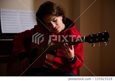 Teenage Boy Playing Acoustic Guitar In A Quiet Room With Sheet Music Backdrop Teenage Boy Playing Acoustic Guitar In A Quiet Room With Sheet Music Backdrop 135923529