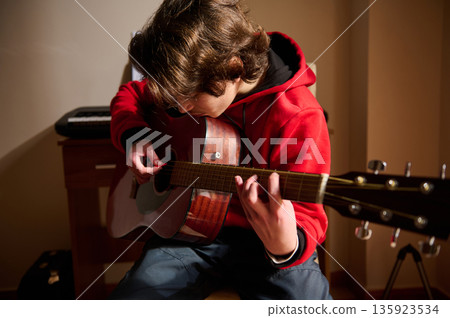 Young Teen Boy In Red Hoodie Playing Acoustic Guitar In A Cozy Home Studio 135923534
