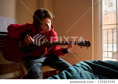 Teenage Boy Plays Acoustic Guitar In Sunlit Room, Quiet Home Music Practice Moment Teenage Boy Plays Acoustic Guitar In Sunlit Room, Quiet Home Music Practice Moment 135923541