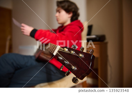 Teen Guitar Player Enjoys Music Hobby At Home In Red Hoodie Teen Guitar Player Enjoys Music Hobby At Home In Red Hoodie 135923548