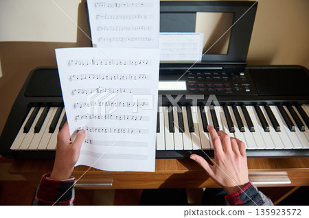 Teenage Pianist Playing Keyboard With Sheet Music On Stand And Hands On Keys 135923572