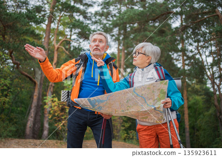 Hiking tourism. Senior couple man woman looking track in paper map enjoying hiking in forest. Happy old people backpackers hikers enjoy walking hike trekking tourism active vacation beauty of nature Hiking tourism. Senior couple man woman looking track in paper map enjoying hiking in forest. Happy old people backpackers hikers enjoy walking hike trekking tourism active vacation beauty of nature 135923611