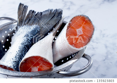 Fresh fish tails in a silver colander on white marble surface ready for preparation in kitchen Fresh fish tails in a silver colander on white marble surface ready for preparation in kitchen 135923803
