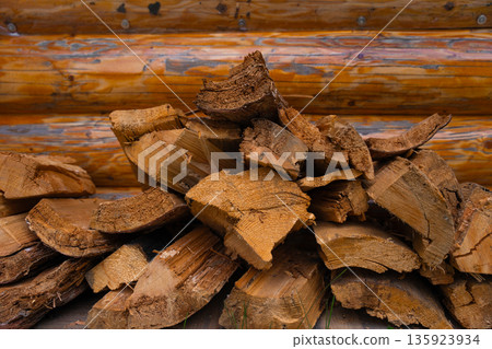 Stack of split firewood in front of wooden cabin wall - natural fuel storage for heating, no people 135923934