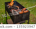 Grilling sausages over open fire on metal barbecue grill in backyard with green grass in autumn 135923947
