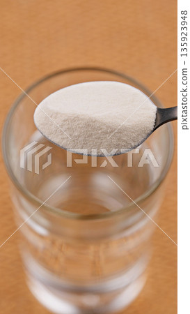 Close-up Spoon Collagen Protein Powder and Glass of Water. Concept of dietary supplement, healthy lifestyle, nutrition, beauty care and soluble wellness product preparation. Food for wellbeing 135923948