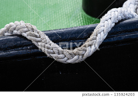 Close up of a braided rope handle attached hanging on a black boat side with a green textured floor Close up of a braided rope handle attached hanging on a black boat side with a green textured floor 135924203
