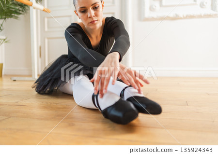 Young ballerina in tutu skirt stretching practicing ballet positions dancing in dance class. Young classical dancer woman in dance studio. Ballet class training Ballet school concept Young ballerina in tutu skirt stretching practicing ballet positions dancing in dance class. Young classical dancer woman in dance studio. Ballet class training Ballet school concept 135924343