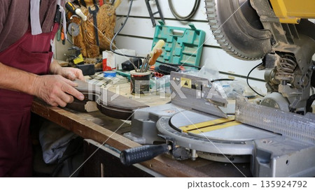 A carpenter holds a curved wooden piece on the work surface of a workbench and prepares to cut the wood material on a miter saw, processing on an end-cutting unit with wood products 135924792