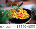 Fresh colorful corn salad with cherry tomatoes, bell pepper, green onions and herbs served in a black bowl on a rustic table. Healthy vegan summer side dish with vibrant vegetables and natural light. 135924855