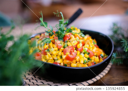 Fresh colorful corn salad with cherry tomatoes, bell pepper, green onions and herbs served in a black bowl on a rustic table. Healthy vegan summer side dish with vibrant vegetables and natural light. Fresh colorful corn salad with cherry tomatoes, bell pepper, green onions and herbs served in a black bowl on a rustic table. Healthy vegan summer side dish with vibrant vegetables and natural light. 135924855