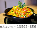 Fresh colorful corn salad with cherry tomatoes, bell pepper, green onions and herbs served in a black bowl on a rustic table. Healthy vegan summer side dish with vibrant vegetables and natural light. 135924856