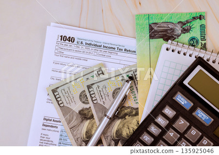Cash dollar bills, tax return 1040 forms, calculator are on table this scene is common during tax filing time. 135925046
