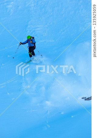 Freeride skier jumping over the cliff fresh powder on a steep slope in blue jacket and green helmet Freeride skier jumping over the cliff fresh powder on a steep slope in blue jacket and green helmet 135925059
