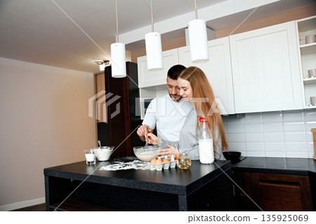 Couple prepares breakfast together in a modern kitchen during a morning at home with eggs and milk on the counter Couple prepares breakfast together in a modern kitchen during a morning at home with eggs and milk on the counter 135925069