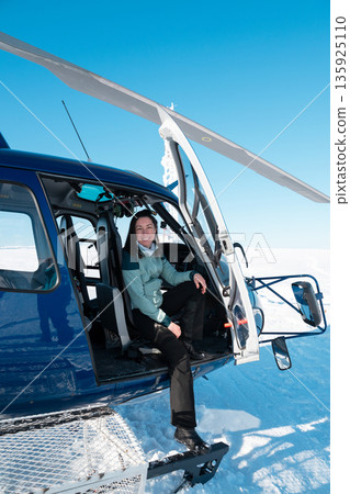 Woman sits in a blue helicopter at the snowy mountaintop, ready for a winter adventure 135925110